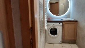 A compact bathroom with a washing machine, a sink, and a mirror with a circular light. - Superb new apartment, nice and functional. Heartwarming welcome.  (Saint-Gervais-Les-Bains)