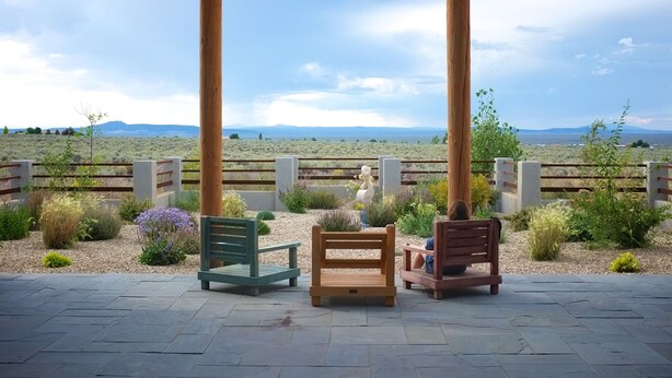 Un patio techado con dos sillas de madera y una mesita, con vistas a un paisaje desértico y montañas al fondo.