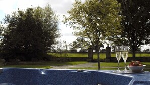 A hot tub with a blue mosaic finish, surrounded by a garden with trees and a fence. - The Cotswold Manor Grange, Exclusive Hot Tub, Games Barn, 70 acres of Parkland (Bampton)