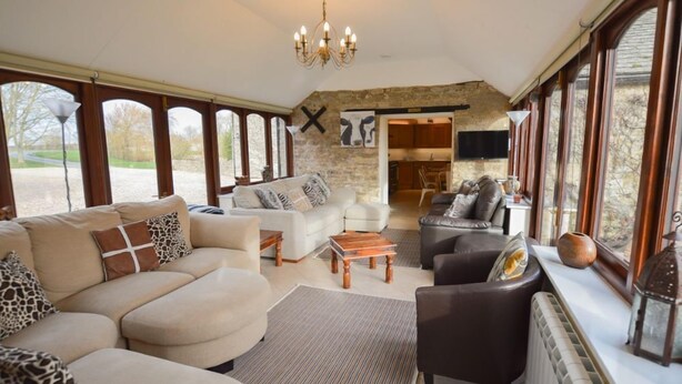 A spacious living area with a stone wall, large windows, and a fireplace. - The Cotswold Manor Grange, Exclusive Hot Tub, Games Barn, 70 acres of Parkland (Bampton)