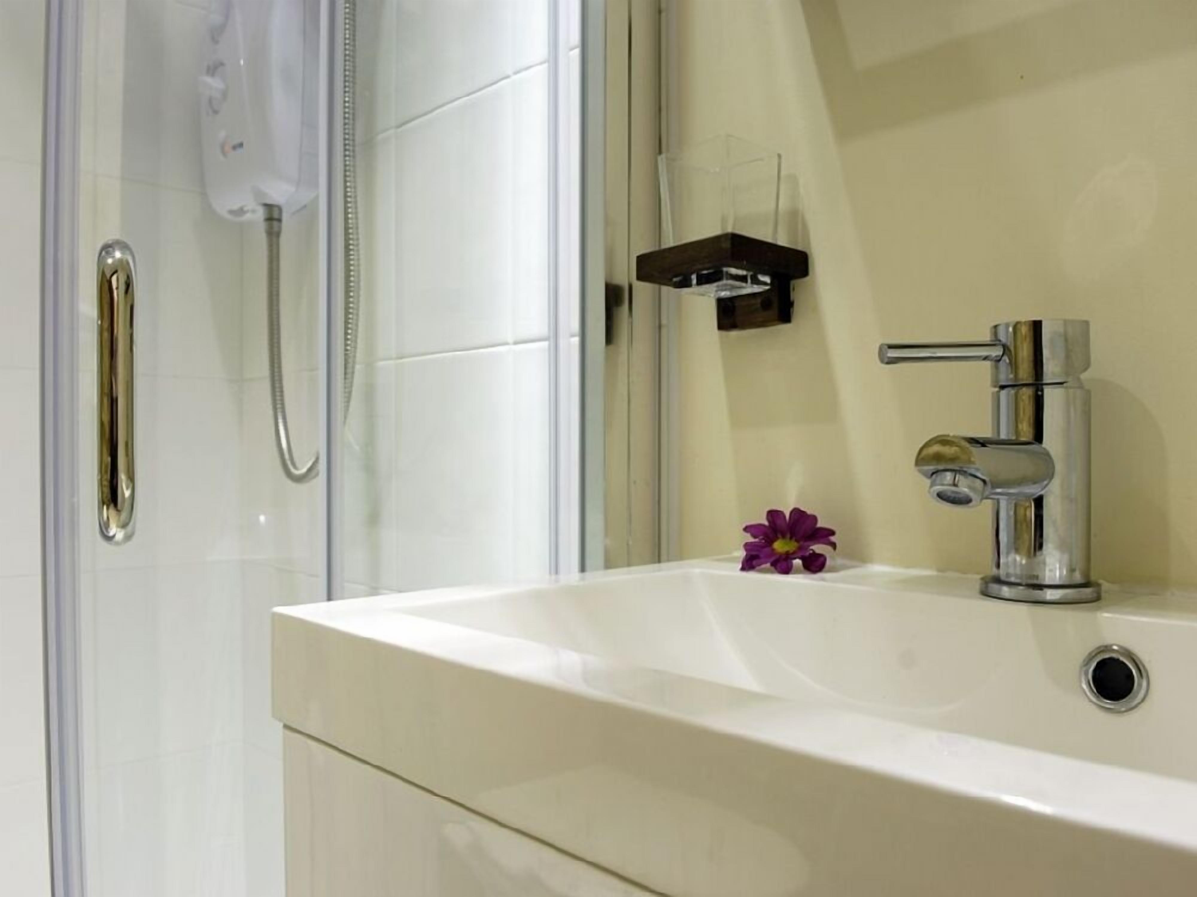 Een badkamer met een wit wastafel, een handdouche en een klein bloemetje op het aanrecht.