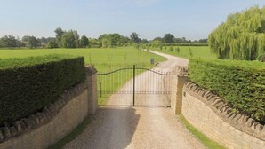 A rural road leading to a gated entrance surrounded by stone walls and hedges. - The Cotswold Manor Grange, Exclusive Hot Tub, Games Barn, 70 acres of Parkland (Bampton)
