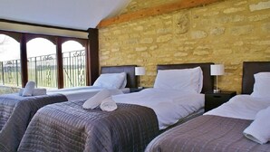 A hotel room with three beds, each with a headboard and a nightstand with a lamp. The room has a stone wall and a balcony with a wrought iron railing. - The Cotswold Manor Grange, Exclusive Hot Tub, Games Barn, 70 acres of Parkland (Bampton)