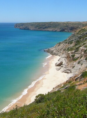 A coastal landscape with a beach, rocky cliffs, and clear blue sea.
