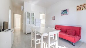 Uma sala de estar moderna com uma mesa de jantar branca, sofá vermelho e uma cozinha com armários e geladeira.
