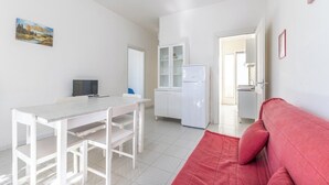 Um espaço compacto com uma mesa de jantar, um sofá vermelho, um armário branco e uma televisão.