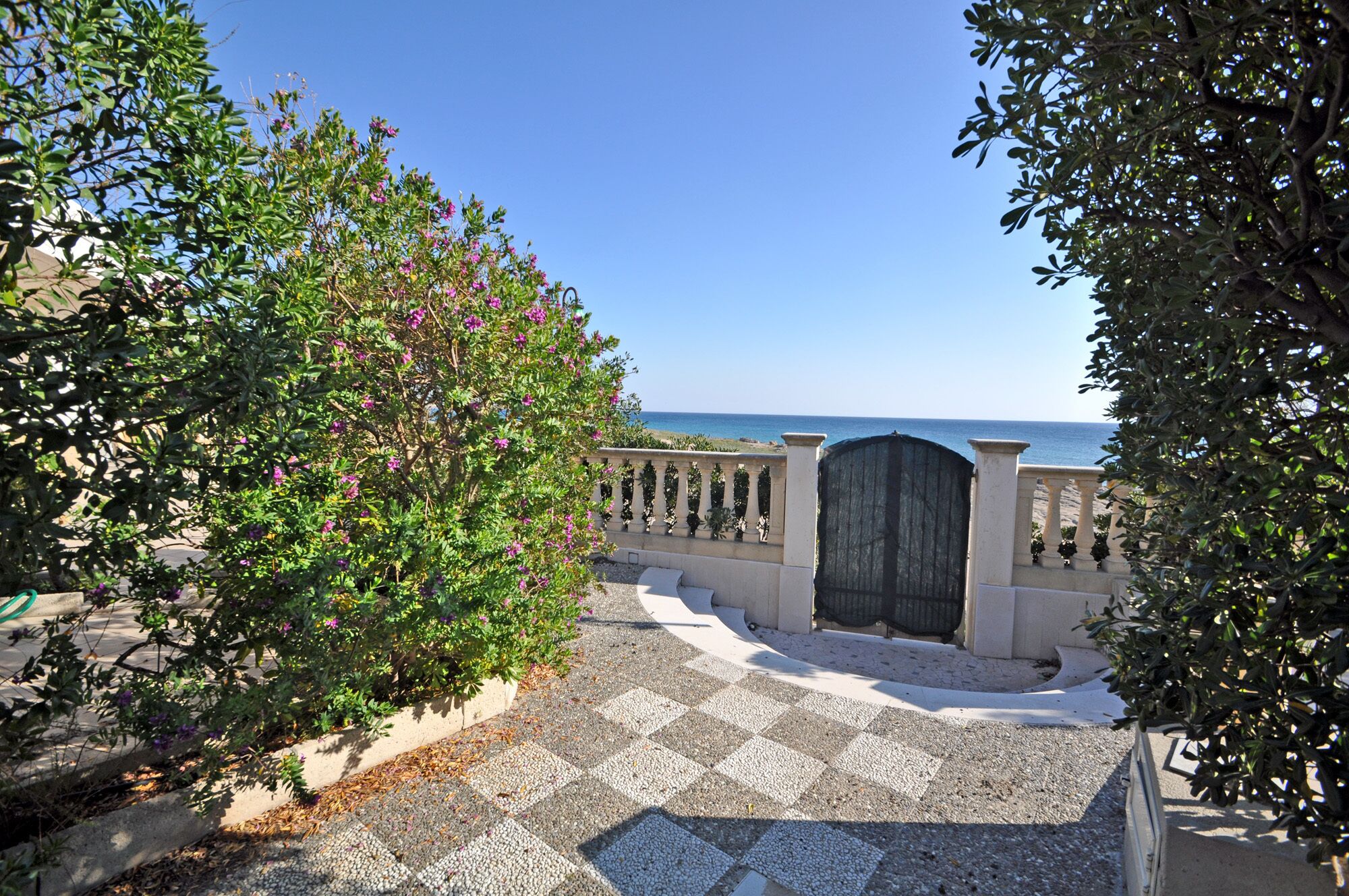 A paved pathway leading to a gate with a view of the sea.