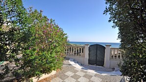 Uma trilha pavimentada conduz a um portão, com vista para o mar.