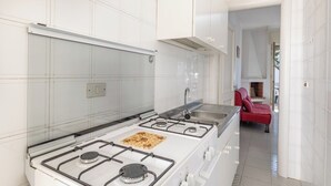 Cozinha moderna com armários brancos, fogão a gás e um sofá vermelho na área de estar adjacente.