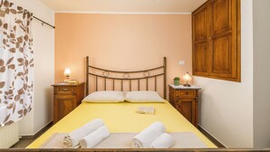 Une chambre à coucher comprenant un lit, deux tables de chevet, une armoire en bois et un rideau orné d’un motif de feuilles.