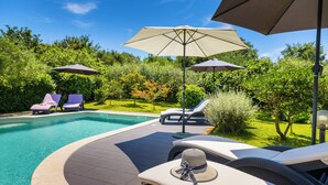 Un espace aménagé au bord de la piscine, avec des chaises longues, des parasols et un petit jardin.