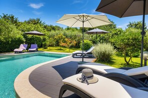 A poolside area with lounge chairs, umbrellas, and a small garden. - Authentic Istrian House - Family Apartment with saltwater pool - near Kamenjak (Pula)