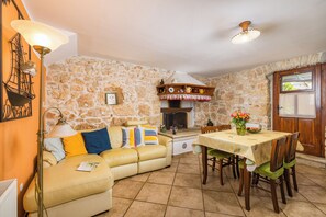 A cozy living room with a stone wall, a sofa with colorful cushions, a dining table with chairs, and a fireplace. - Authentic Istrian House - Family Apartment with saltwater pool - near Kamenjak (Pula)