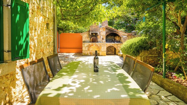 Un espace de restauration en plein air avec une table dressée pour deux personnes, entouré de murs en pierre et de verdure.