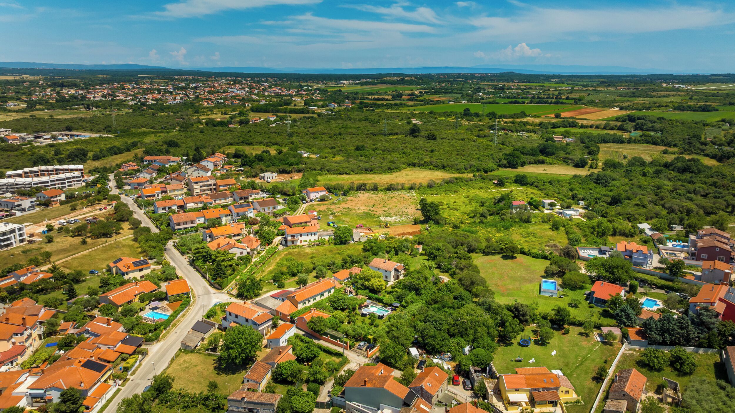 A residential area with houses, roads, and green fields.