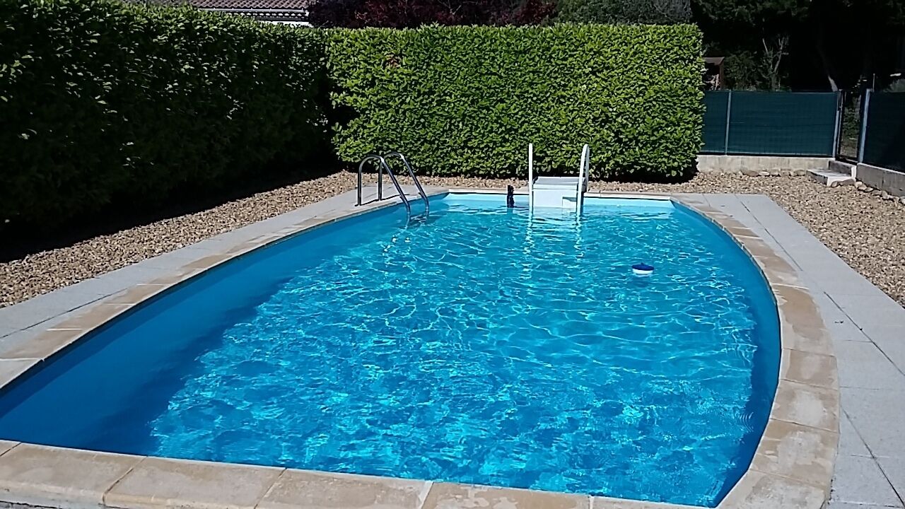 A rectangular swimming pool with clear blue water, surrounded by a stone border.