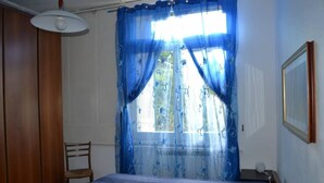 Een slaapkamer met een bed, een stoel, een nachtkastje, een lamp en een raam met blauwe gordijnen.