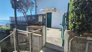 Een landhuis aan de kust met een stenen trap die leidt naar een groene deur, een beveiligingscamera en een bord met een melding van cameratoezicht.