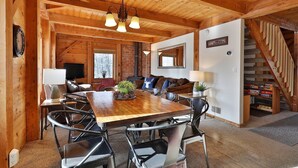Accogliente interno di una baita in legno con un tavolo da pranzo in legno, sedie, un caminetto, un divano e una scala.