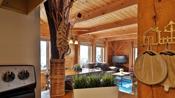 Un accogliente interno di una baita con soffitto in legno, zona pranzo con tavolo e sedie, un divano, una televisione e un caminetto.