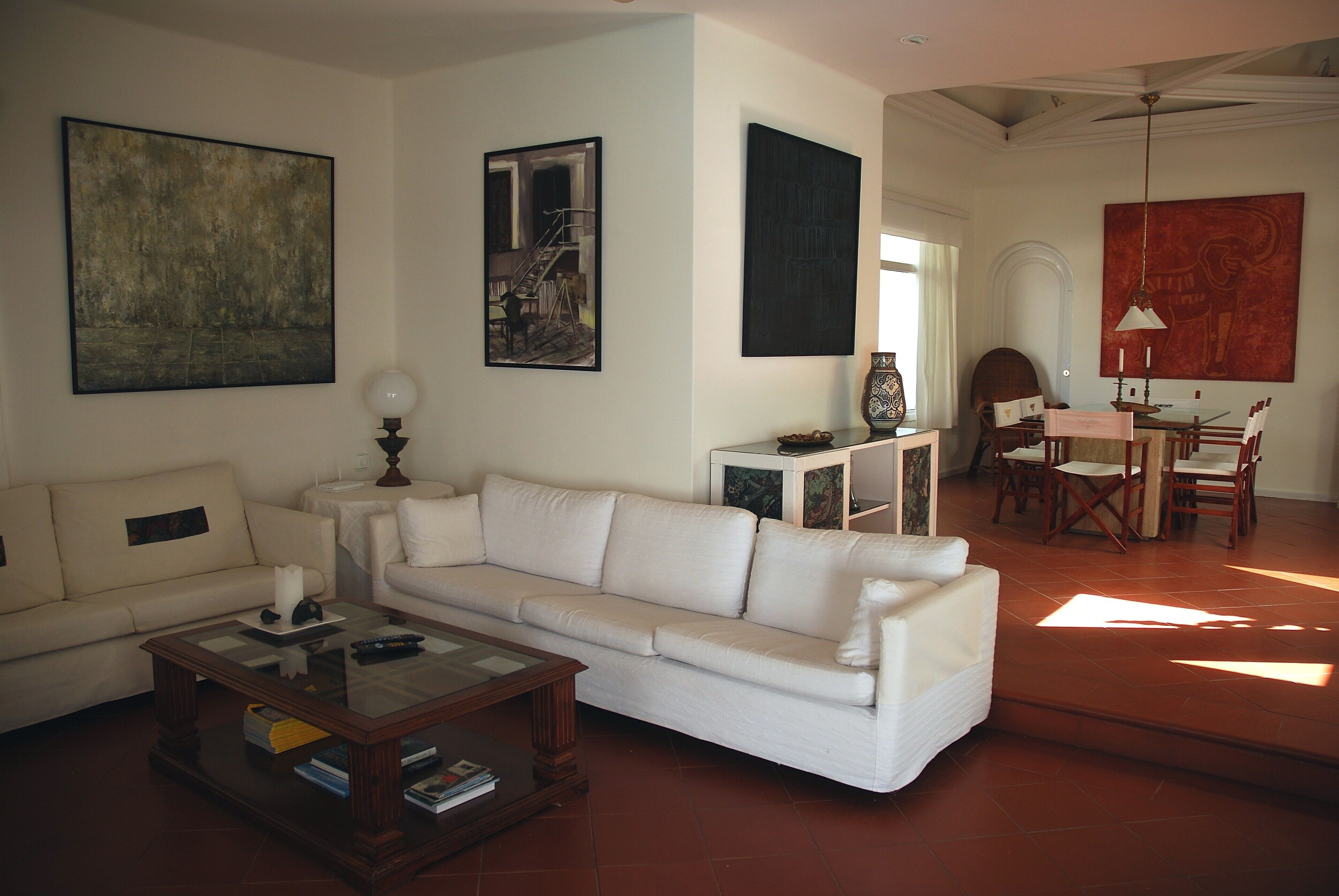 Uma sala de estar com sofá branco, mesa de centro de vidro e um espaço de jantar com mesa e cadeiras.