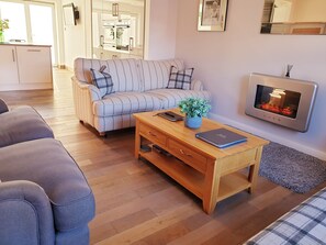 A living room with a sofa, a wooden coffee table, a fireplace, and a kitchen in the background.