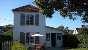 A two-story house with a white exterior and a red-tiled roof. There is a patio with a table and chairs, and a white umbrella.