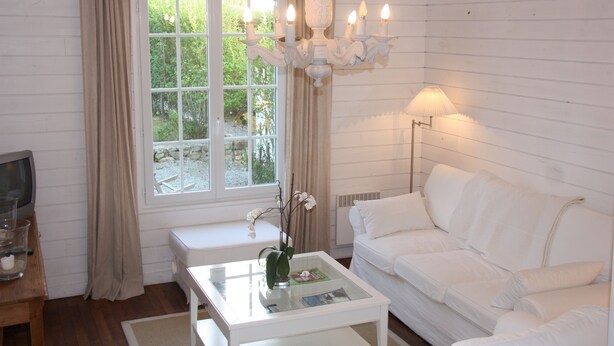A white room with a white sofa, a glass coffee table, a TV, and a window with curtains.