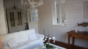 A white wooden room with a white sofa, a glass coffee table, a chandelier, and a wooden side table with a fish sculpture.