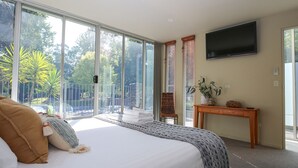 A bedroom with a large bed, a TV mounted on the wall, and a balcony with a view of trees and a fence. - THE GLASS PINNACLE : Bright (Bright)
