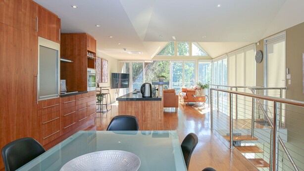 A modern kitchen with wooden cabinets, a dining area with a glass table, and a view of the outdoors through large windows. - THE GLASS PINNACLE : Bright (Bright)