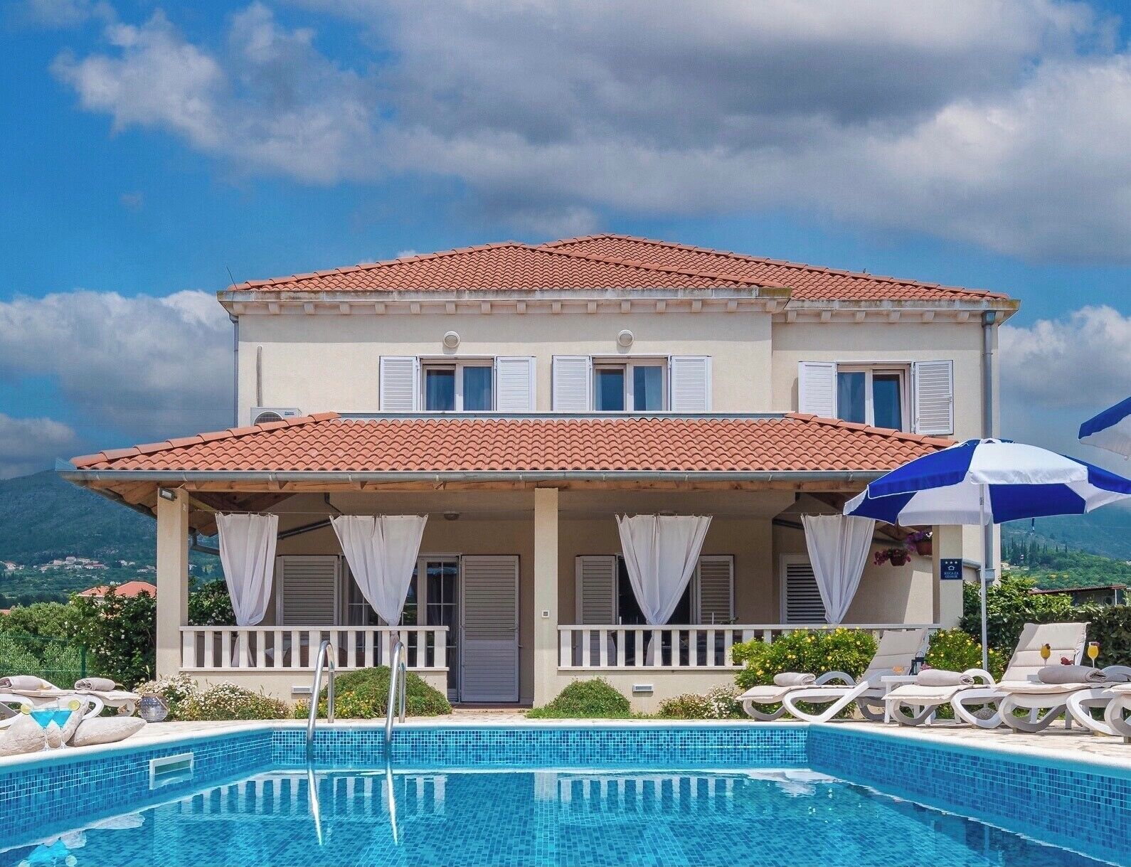 Ein zweistöckiges Gebäude mit Pool, weißen Fensterläden und einem roten Ziegeldach.
