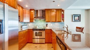 A kitchen with wooden cabinets, stainless steel appliances, a tiled backsplash, and a granite countertop. - Bayfront Balcony, beach access, parking, bikes (San Diego)