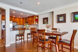 A dining area with a wooden table and chairs, a kitchen in the background, and a framed picture on the wall. - Bayfront Balcony, beach access, parking, bikes (San Diego)