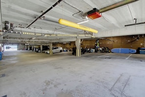 A multi-level parking garage with concrete floors and walls, featuring overhead lighting and a yellow clearance sign.