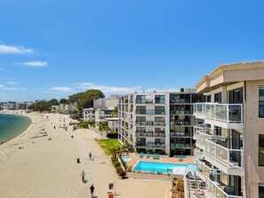 A beachfront hotel with a pool, multiple balconies, and a sandy beach.