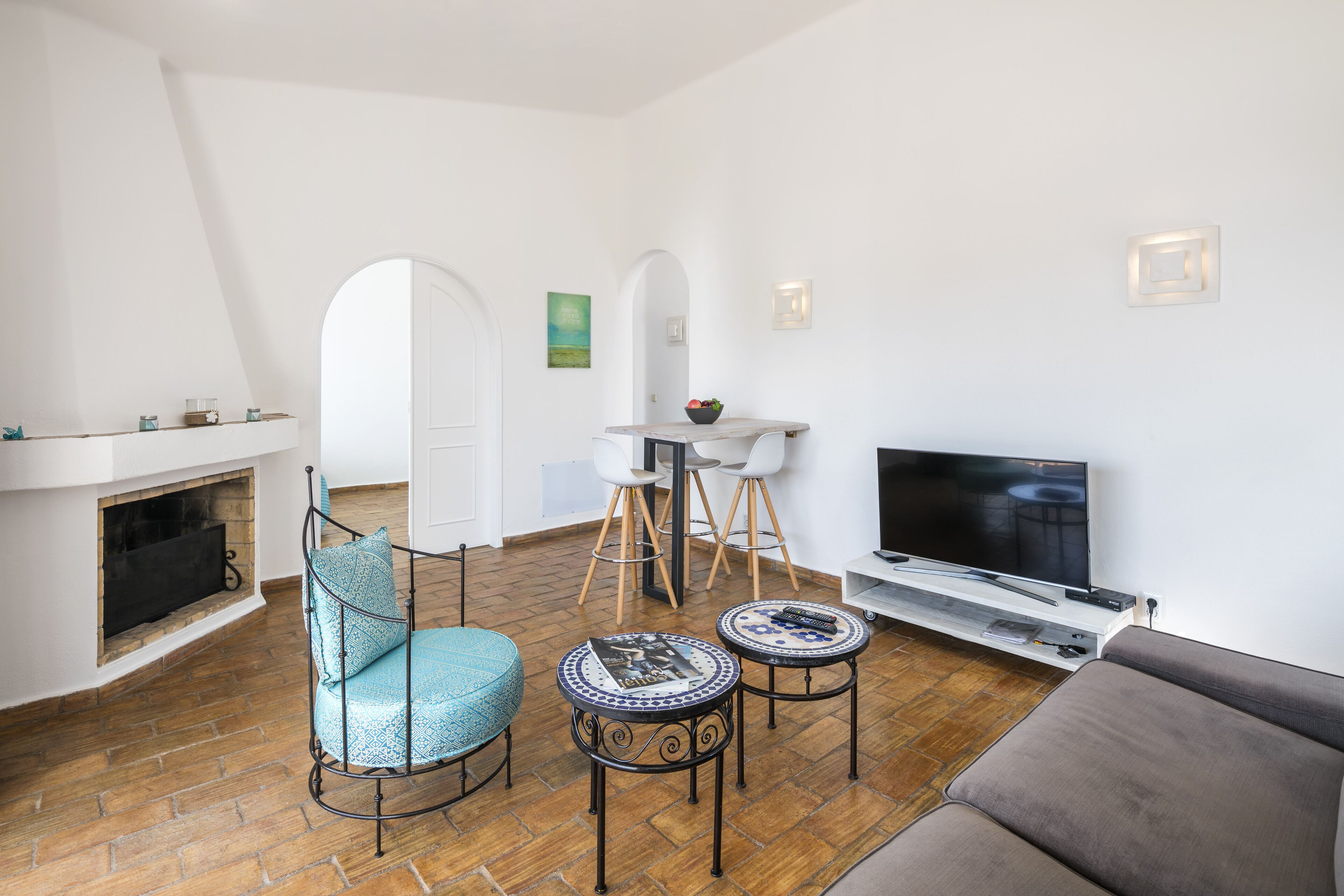 A living room with a fireplace, a sofa, a TV, and two bar stools.
