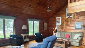 L’intérieur d’un chalet accueillant, avec un revêtement mural en bois, un canapé, un fauteuil, une table basse et un escalier.