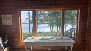 Une pièce de cabane en bois avec une grande fenêtre donnant sur un lac et une forêt.