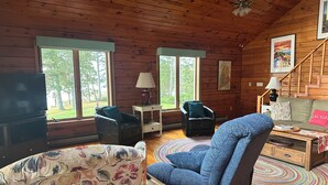 L’intérieur d’un chalet accueillant, avec des murs en bois, un canapé, deux fauteuils, une table basse et un téléviseur.