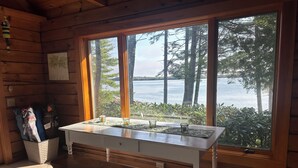 Une cabane en bois dotée d’une grande fenêtre donnant sur un lac, une table avec des verres et un banc.