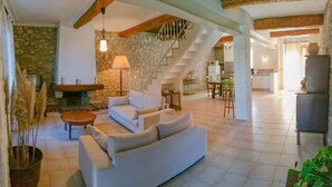 A spacious living area with a white sofa, a stone fireplace, a staircase, and a kitchen in the background. - Nice confortable cottage with large pool with views in minervois  (Montbrun-Des-Corbières)