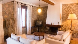 A living room with a stone wall, a fireplace, a television, and two sofas. - Nice confortable cottage with large pool with views in minervois  (Montbrun-Des-Corbières)
