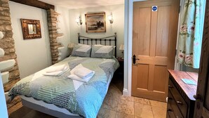 Une chambre avec un mur d’accent en pierre, un lit avec une literie à motifs, un tableau au-dessus du lit, une porte en bois avec une inscription et une petite commode.