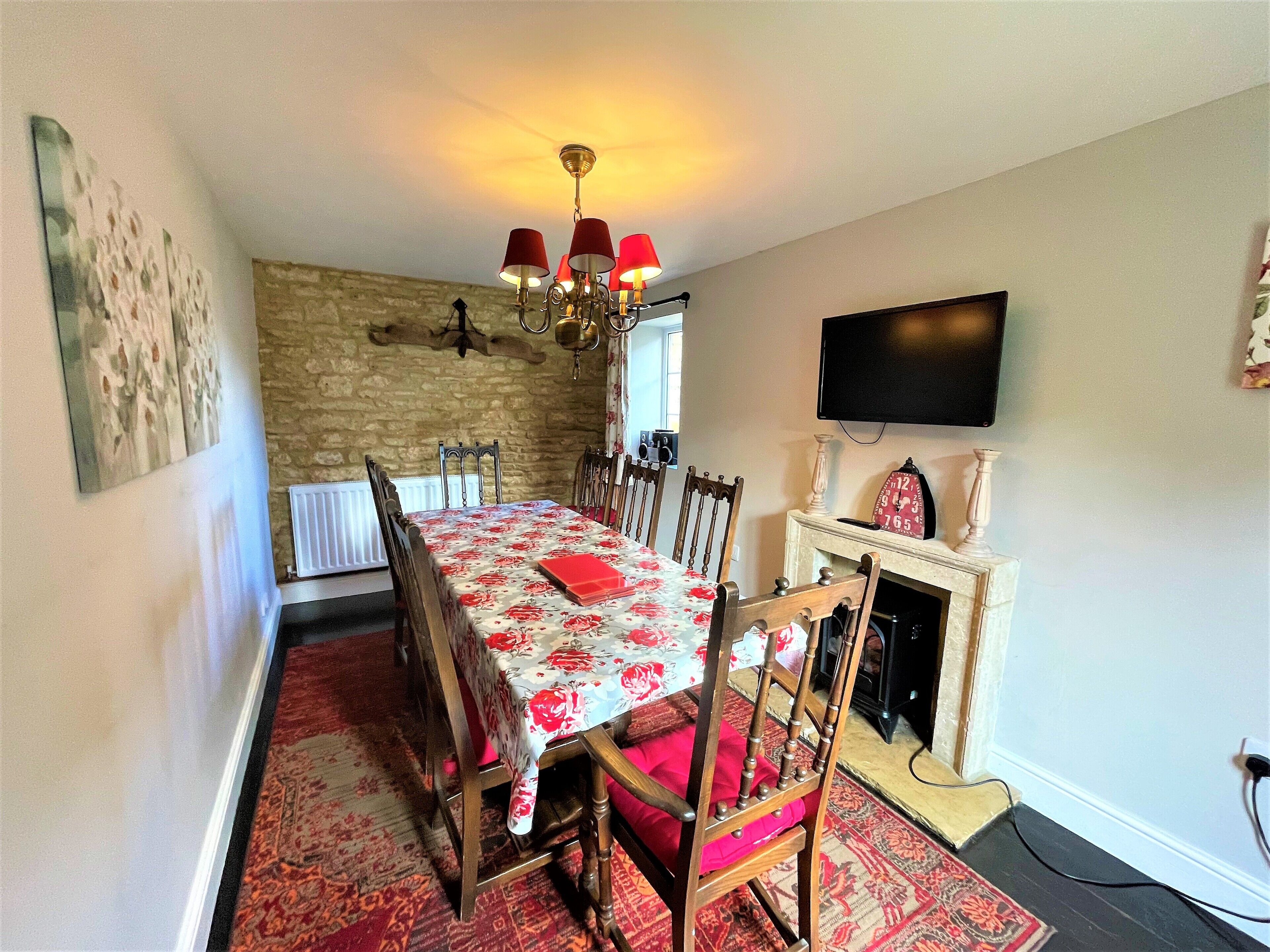 A dining room with a long table, chairs, a chandelier, a fireplace, and a television mounted on the wall.