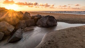 Una spiaggia con grandi rocce, un mare calmo e un tramonto.