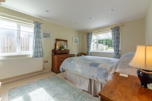 A bedroom with a bed, a dresser, a nightstand, a lamp, and a window with curtains. - Betty's Cottage, Brancaster, Norfolk (Brancaster)