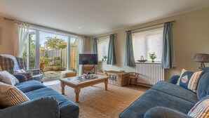 Un soggiorno con divano, tavolino, televisione e vista sul giardino attraverso ampie finestre.