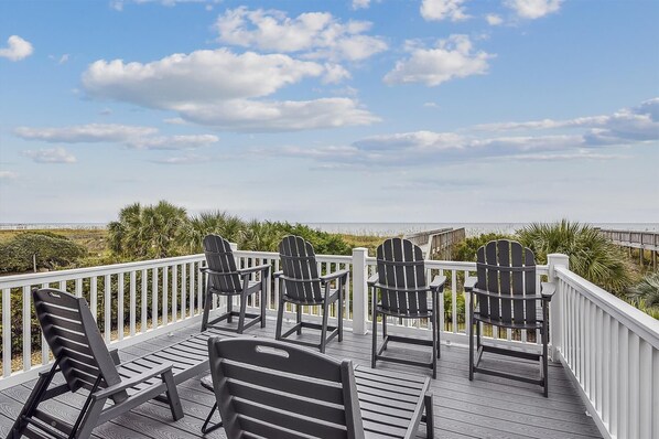 A deck with Adirondack chairs and a bench, overlooking a beach with a wooden boardwalk and palm trees. - Beach Life, 8 bedroom Oceanfront with Pool (NORTH MYRTLE BEACH)