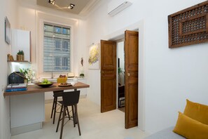 Une cuisine moderne avec un plan de travail en bois, un coin repas avec une chaise noire et un coussin jaune vif dans l’espace de vie.